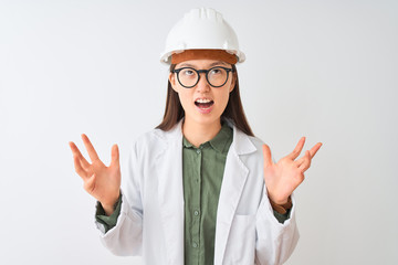 Sticker - Young chinese engineer woman wearing coat helmet glasses over isolated white background crazy and mad shouting and yelling with aggressive expression and arms raised. Frustration concept.