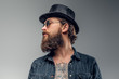 Serious bearded man in hat and sunglasses is posing at photo studio.