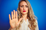 Fototapeta  - Young beautiful woman wearing striped shirt standing over blue isolated background with open hand doing stop sign with serious and confident expression, defense gesture