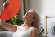 Exhausted older woman waving fan close up, suffering from heat