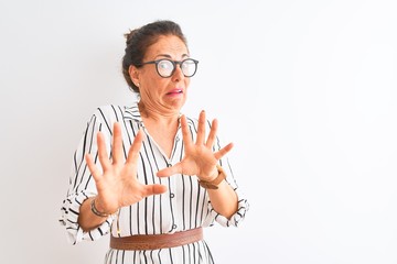 Wall Mural - Middle age businesswoman wearing striped dress and glasses over isolated white background afraid and terrified with fear expression stop gesture with hands, shouting in shock. Panic concept.