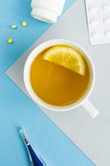 Cold and flu season. Cup with hot tea and lemon, thermometer, pills on a light background. Treatment and prevention of the virus. 