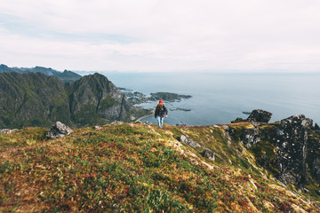 Wall Mural - Traveler man wearing backpack and red hat climb on high mountains above sea. Professional expeditor standing on the edge cliff rock and looking forward away. Wanderlust