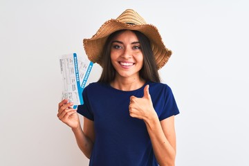 Wall Mural - Young beautiful tourist woman holding boarding pass ticket over isolated white background happy with big smile doing ok sign, thumb up with fingers, excellent sign