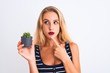 © Krakenimages.com - Young beautiful woman holding small cactus pot standing over isolated white background serious face thinking about question, very confused idea