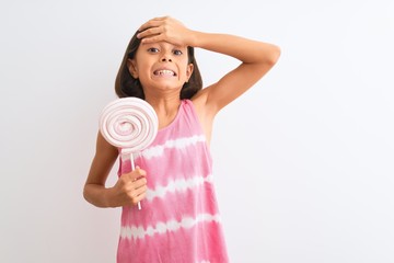 Poster - Beautiful child girl eating sweet lollipop standing over isolated white background stressed with hand on head, shocked with shame and surprise face, angry and frustrated. Fear and upset for mistake.