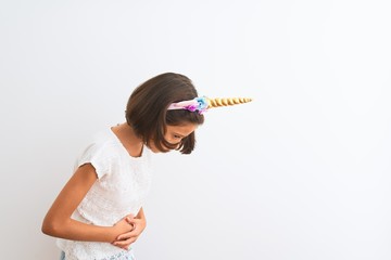 Sticker - Beautiful child girl wearing unicorn diadem standing over isolated white background with hand on stomach because indigestion, painful illness feeling unwell. Ache concept.