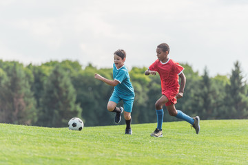 Wall Mural - excited multicultural kids playing football on grass