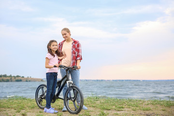 Canvas Print - Woman and her little daughter with bicycle near river