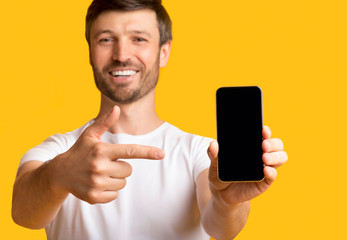 Poster - Man Holding Smartphone Pointing Finger At Screen, Yellow Background