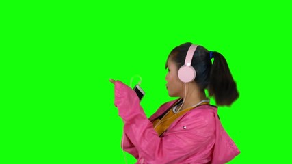 Wall Mural - Attractive woman enjoying music with a mobile phone and headphones while dancing in the studio. Shot in 4k resolution with green screen background