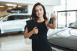 © studioprodakshn - beautiful brunette woman manager holding brochure in one hand and car keys in another standing in dealership center