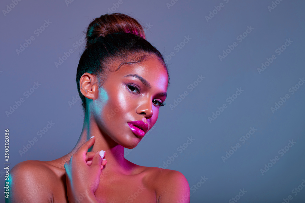 Beauty Porter young dark skinned Girl with perfect skin and makeup. Bridal Makeup - delicate pink tones, wet make-up, shine. Sexy plump lips. Hair gathered in the bun on his head. Neon light. - Image  - obrazy, fototapety, plakaty 