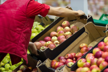 Young man seller lays out fresh fruits of the box on the grocery store