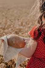Portrait Of Happy Young Woman In Red Dress Holding Rustic Rye Bread On Wheat Field Sun Background