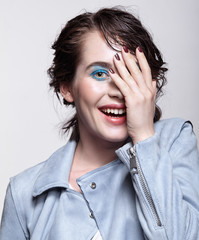 Wall Mural - Portrait of smiling female in blue jacket with hand on face. Woman with unusual beauty makeup and wet hair, and blue shadows make-up.