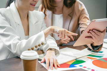 Wall Mural - Closeup Two asian businesswomen working with the partner business by point finger to the technology tablet in modern meeting room, office or working space, coffee break, partner and colleague concept