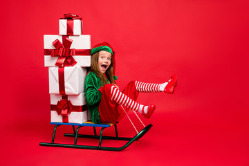 Poster - Profile side view of nice attractive cheerful glad excited funny carefree pre-teen elf sitting on sled carrying delivering fairy miracle tradition isolated over bright vivid shine red background