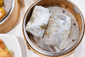 Wall Mural - Delicious Lo Mai Gai dim sum, fresh steamed glutinous rice with chicken roll wrapped by lotus leaf in bamboo steamer in hong kong yumcha restaurant.