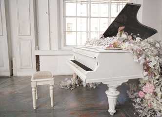 white grand piano with spring white and pink flowers in a white room with nobody