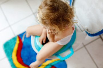 Closeup of cute little toddler baby girl child sitting on toilet wc seat. Potty training for small children. Unrecognizable face of child