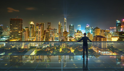 Businessman standing at transparent glass floor on rooftop with night city panoramic view.