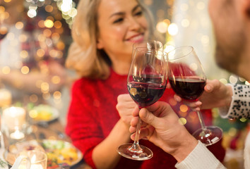 holidays and celebration concept - close up of happy friends having christmas dinner at home, drinking red wine and clinking glasses