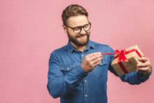 Happy Holiday, My Congredulations! Portrait Of An Attractive Casual Man Giving Present Box And Looking At Camera Isolated Over Pink Background.