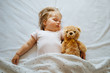© kaloriya - Little baby sleeping on bed hugging soft toy bear, white background