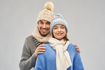 Wall Mural - people, christmas and winter clothes concept - happy couple in knitted hats and scarves over grey background