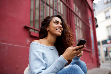 Wall Mural - young Indian woman sitting outside in the city with cellphone in hand