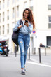 Full length young woman walking with mobile phone and bag in city