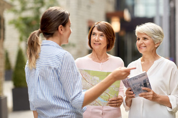 Canvas Print - tourism, travel and friendship concept - female passerby showing direction to senior women with city guide and map on tallinn street