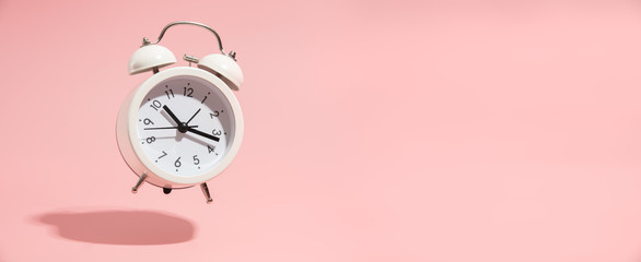 pink alarm clock on pastel pink background.