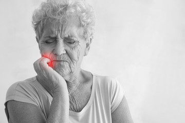 Senior woman suffering from toothache on light background