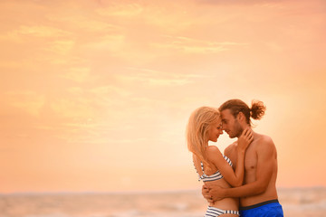 Canvas Print - Young woman in bikini kissing her boyfriend on beach at sunset. Lovely couple