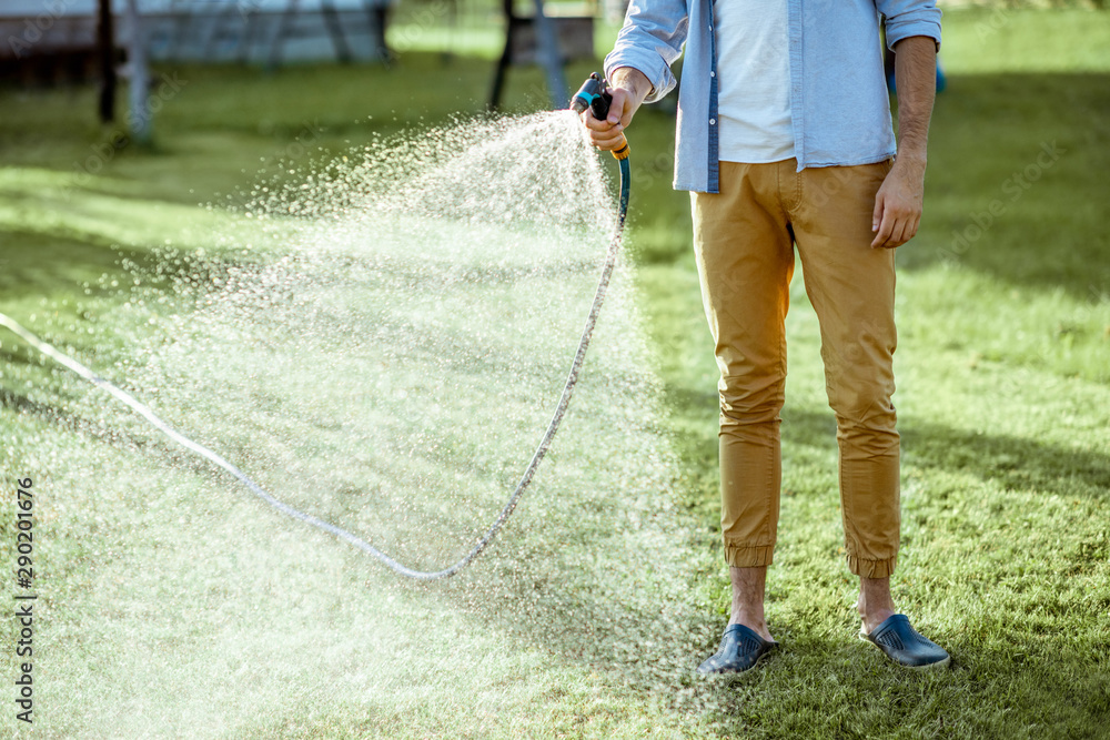 Man watering green lawn, sprinkling water on the grass with water pistol, close-up with no face