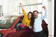 © studioprodakshn - young couple looking for car in dealership center beautiful woman is sticking out the vehicle window handsome man is standing near both with hands up