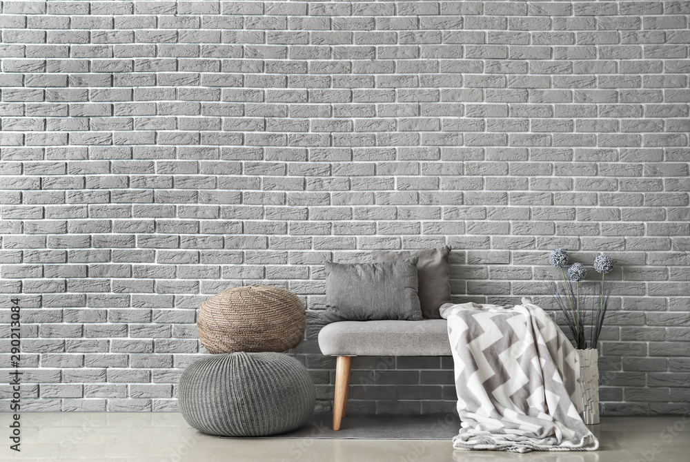 Cozy sofa with poufs near brick wall in room