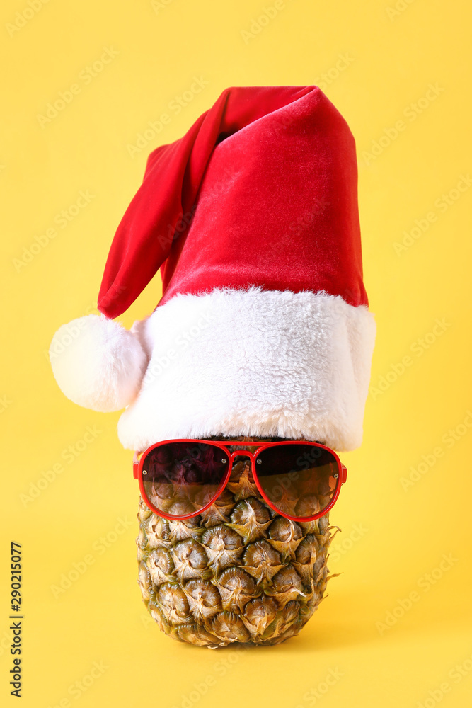 Pineapple with Santa hat and sunglasses on color background
