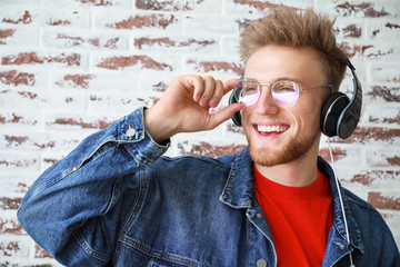 Sticker - Handsome young man listening to music against brick wall