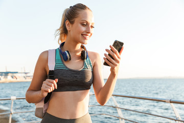 Poster - Beautiful young fitness woman carrying backpack walking at the pier