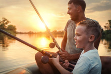 Happy Father And Son Together Fishing From A Boat At Sunset Time