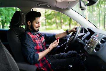 Indian man drive car while hand holding smartphone to use online application.