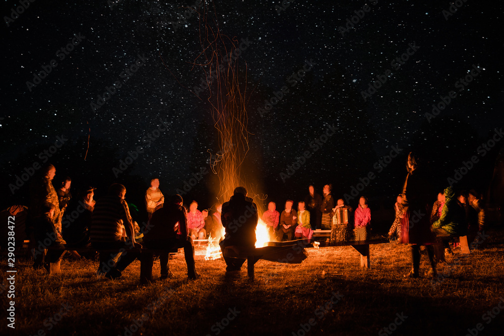 beautiful scenery of night vision. bonfire around people. basking by the fire at night. the concept of outdoor activities. - obrazy, fototapety, plakaty 