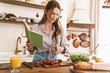 © Drobot Dean - Pretty lady indoors at the kitchen cooking holding notebook.