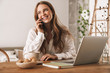 © Drobot Dean - Business woman sit indoors in office using laptop computer taking by mobile phone.