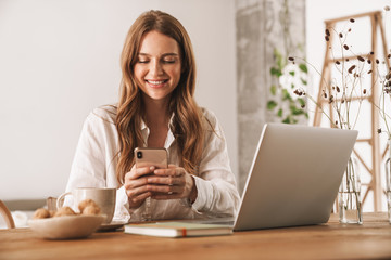 Business woman sit indoors in office using laptop computer and mobile phone.