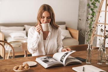 Wall Mural - Woman sit indoors in office reading magazine drinking coffee.