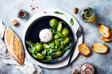 Green zebra tomatoes and burrata cheese salad with fresh arugula, olive oil and toasted bread. Overhead view